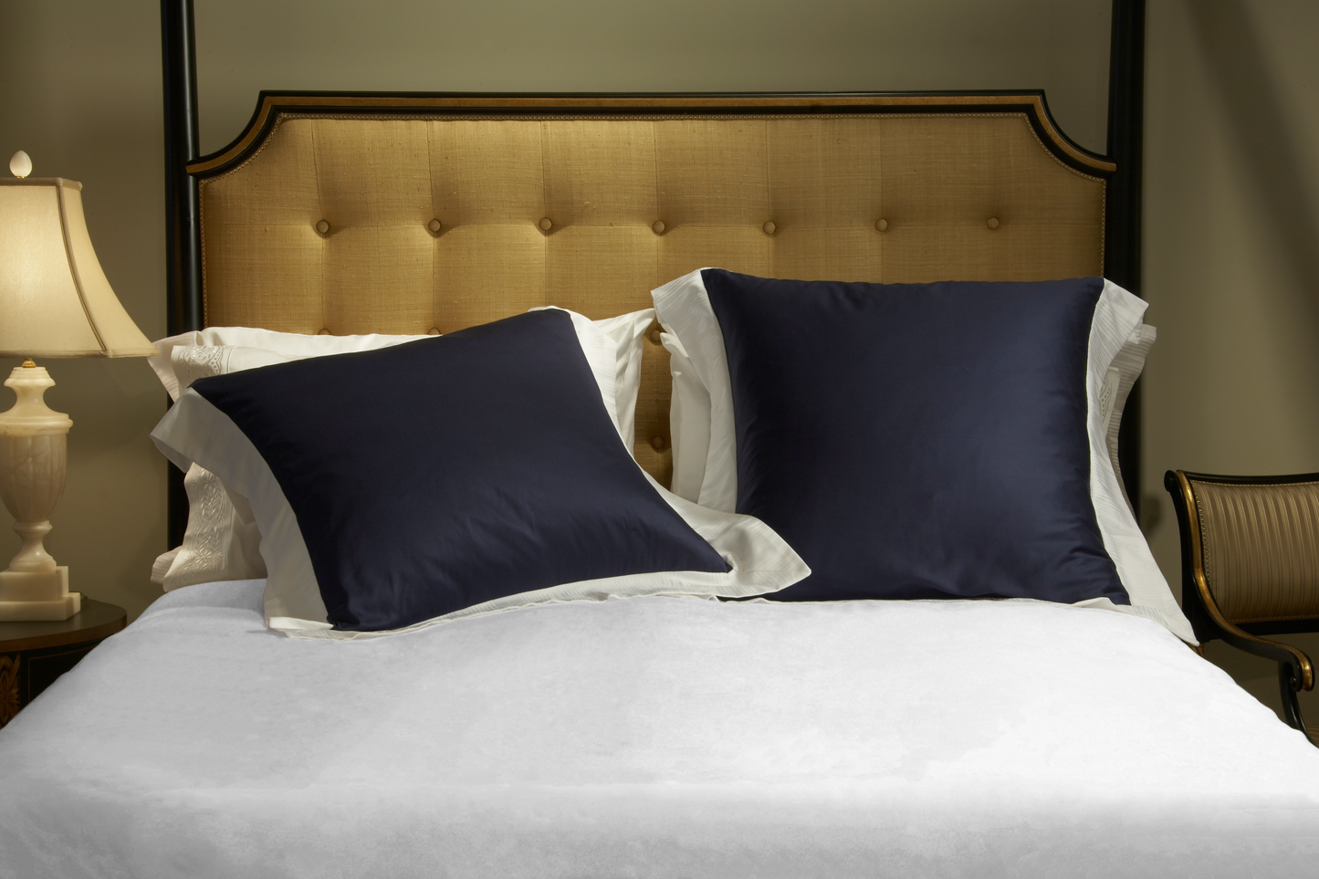 Photo of  a bed by WAB Studios with Two Navy Soleil Sateen Euro Shams with White Soleil Jacquard Borders on 4 sides with a White Soleil Sateen Duvet Cover.  Two queen pillows behind are Kearsley White Essentials Sateen with White Tyrolean II Embroidery on the cuffs.  Woven and made in Italy to the highest ethical, environmental, and craftsmanship standards.  Luxury Linens